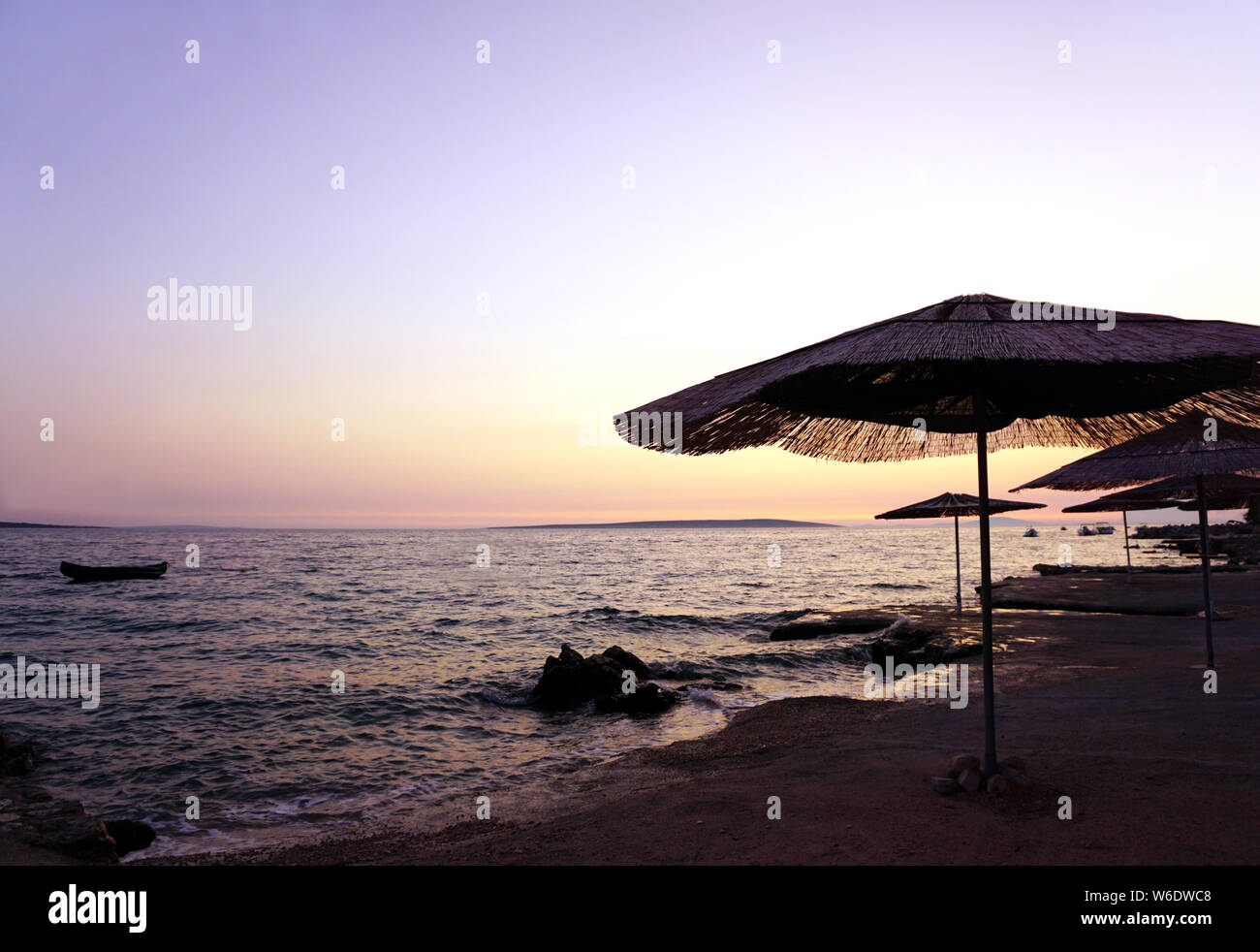Il bambù ombrelloni sulla spiaggia vuota da sul mare al tramonto, con colori pastello del cielo e del mare in una bella serata estiva Foto Stock