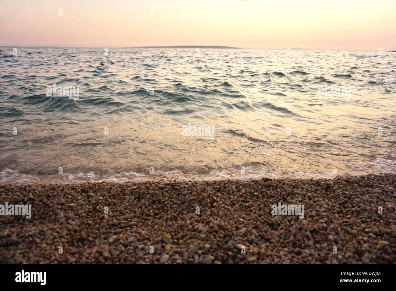 Marea del mare e la turbolenza del mare ondeggiante su una spiaggia di ciottoli al tramonto Foto Stock