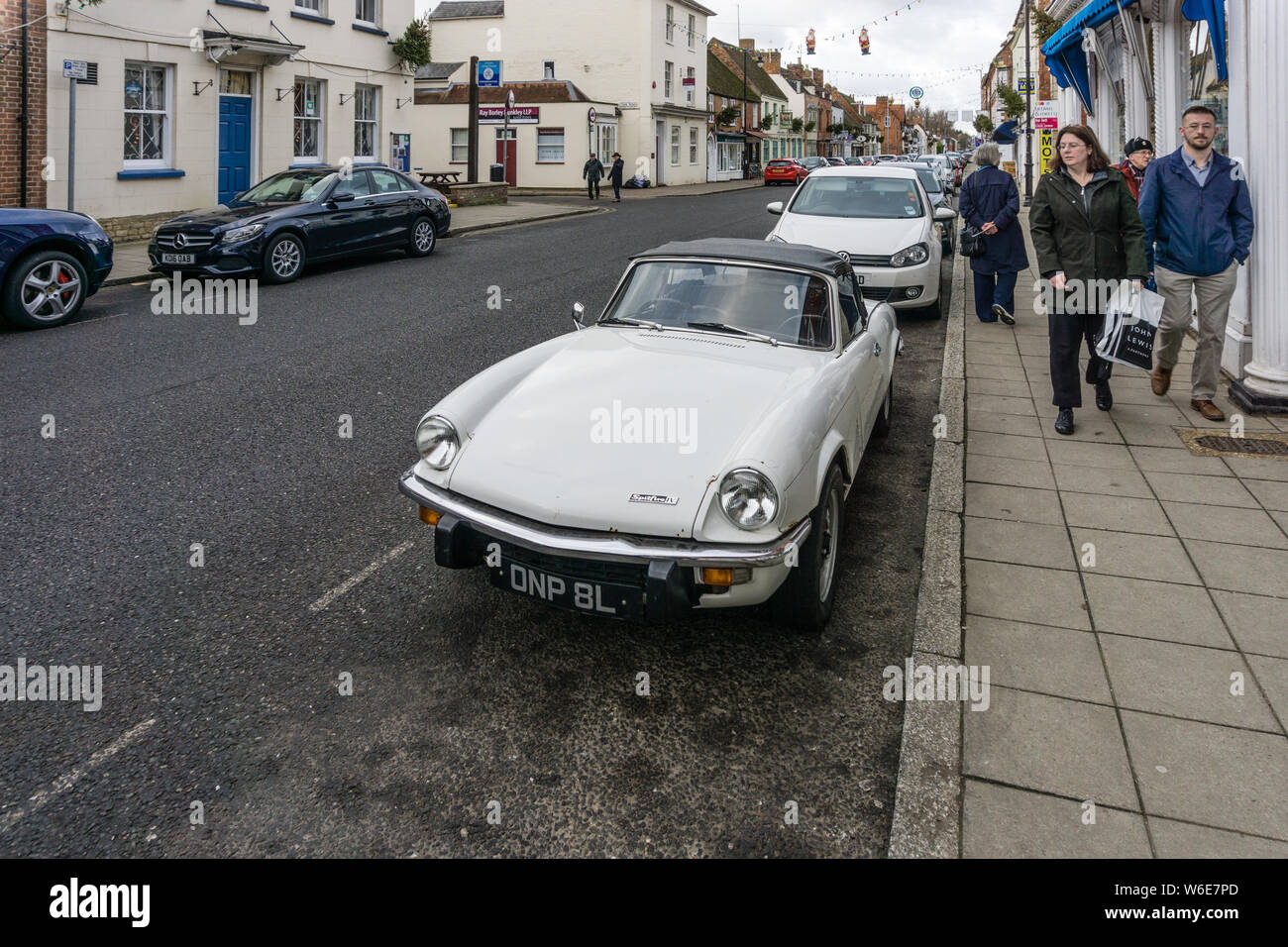 Una donna shopper getta uno sguardo ammirato in un classico bianco Spitfire auto sportiva, High Street, Stony Stratford, Regno Unito Foto Stock