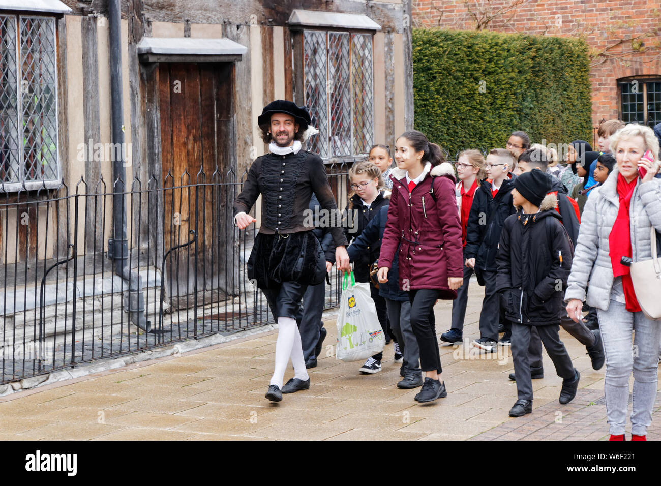 Un uomo vestito da William Shakespeare a piedi attraverso le strade di Stratford upon Avon dato un tour guidato da un gruppo di bambini delle scuole Foto Stock