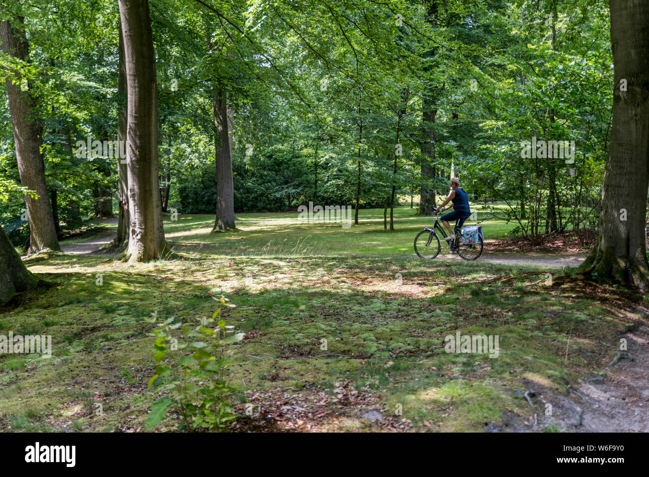 Donna su una bicicletta nel grande giardino con prato verde e il percorso a piedi con un piccolo fiume che attraversa in paesi bassi Foto Stock