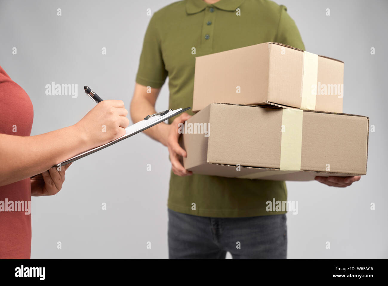 Consegna maschio uomo in verde t shirt tenendo due scatole di cartone. Femmina azienda cliente cartella con i documenti e la firma con la penna. Concetto di consegna rapida. Foto Stock