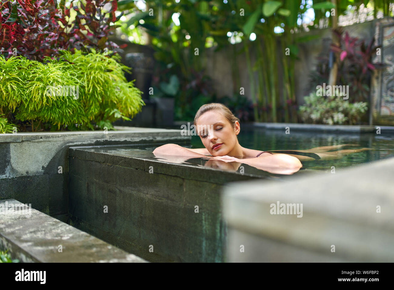 Bella donna tranquillo relax all'aperto nella soleggiata e circondata di piante piscina del lussuoso hotel durante la vacanza tropicale di Bali Foto Stock