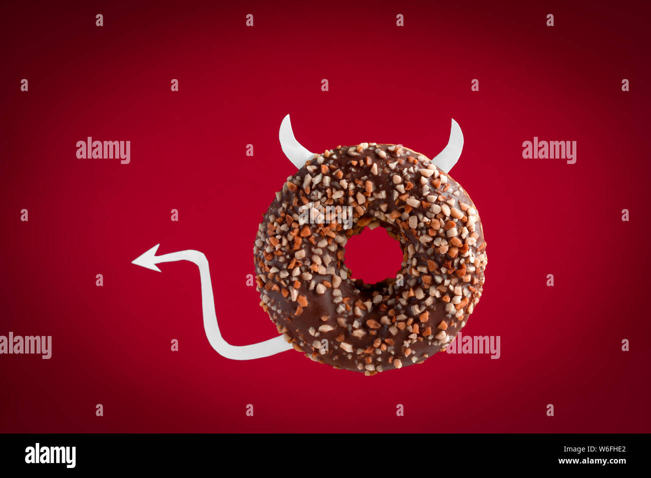 Diavolo di cioccolato ciambella con corna di carta e la coda a volare su sfondo rosso Foto Stock