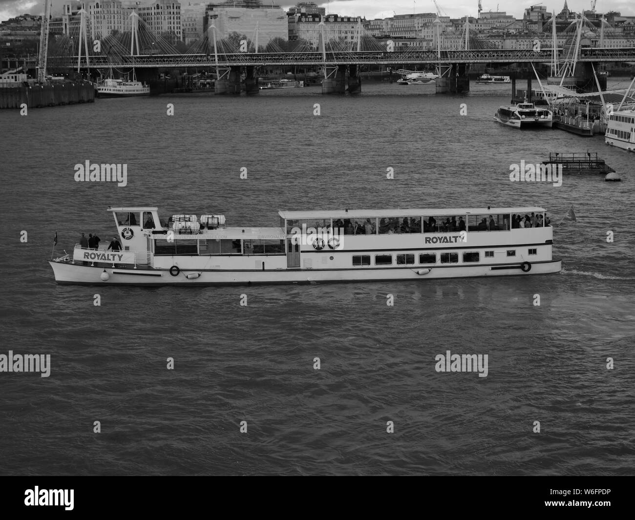 Crociera turistica barca la royalty gira sul fiume Tamigi sul suo viaggio breve viaggio con il Golden Jubilee passerella in background in Londra. Foto Stock
