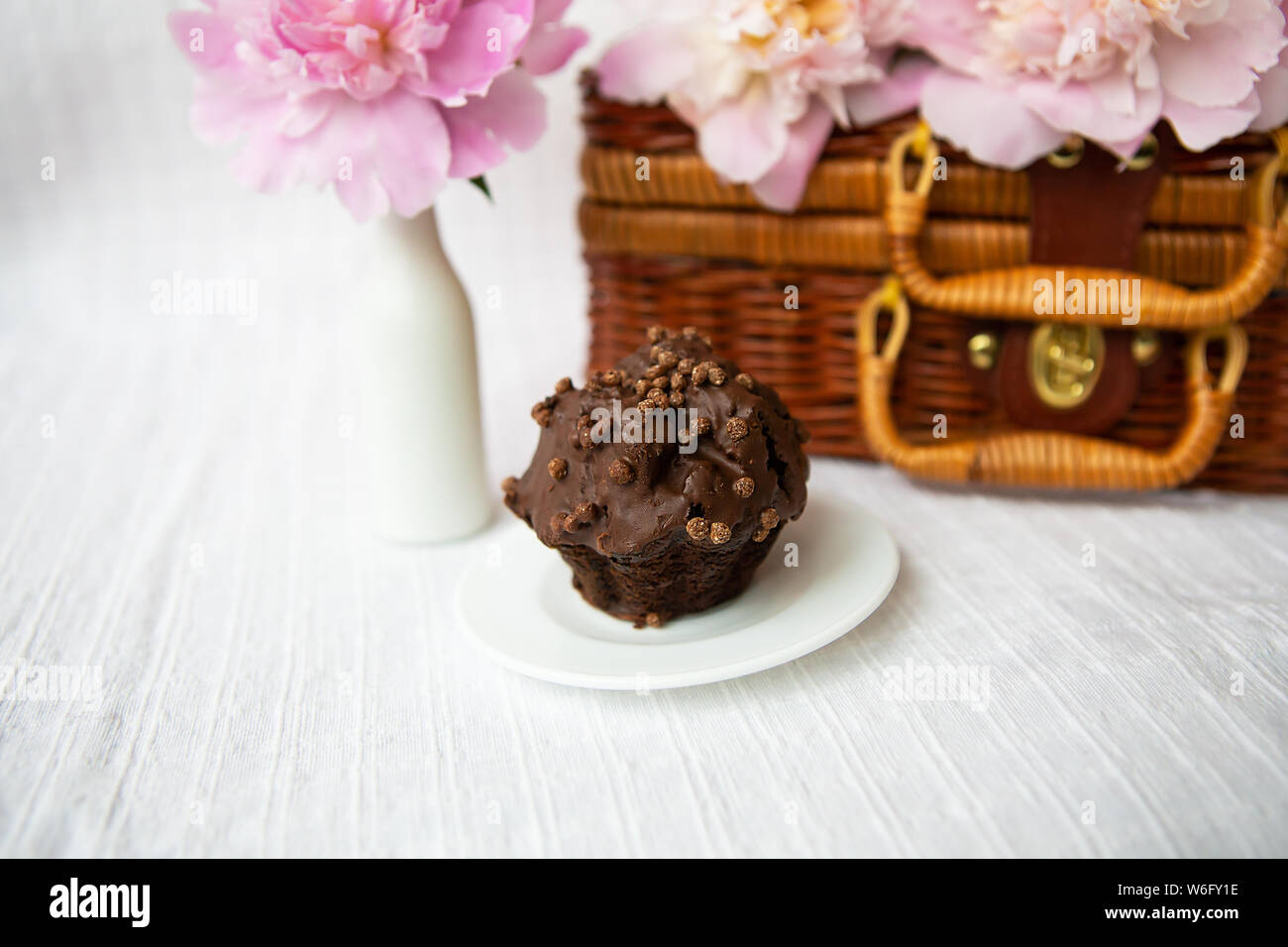 Muffin al cioccolato e di un bel colore rosa peonie giacciono su una valigia di legno. Bella composizione. Foto Stock
