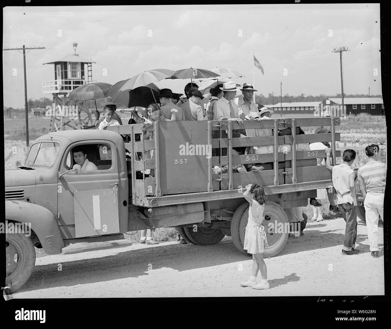 La chiusura del Jerome Relocation Center, Denson, Arkansas. Uno dei molti camion carichi di Girolamo re . . .; Portata e contenuto: tutta la didascalia per questa fotografia si legge: Chiusura del Jerome Relocation Center, Denson, Arkansas. Uno dei molti camion carichi di Girolamo residenti in attesa broiling sun per essere messo sui treni per la loro nuova destinazione. Sullo sfondo le stelle e strisce di body può essere visto volare oltre la caserma militare e a sinistra di uno dei più utilizzati torri di guardia. Foto Stock