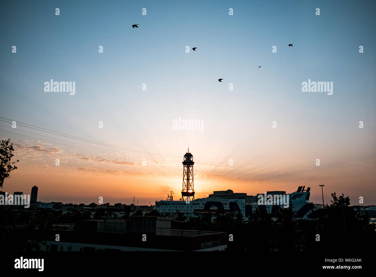 Funivia montjuic torre all'alba con il sorgere del sole dietro la torre durante il sunrise con spettacolari raggi, un punto di riferimento di Barcellona con il porto e la crociera sh Foto Stock