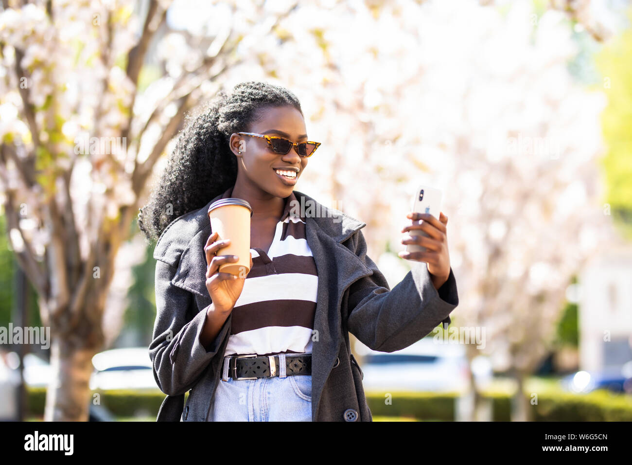 Affascinante afro donna americana con caffè chiacchierando con gli amici nelle reti sociali e navigare su siti internet per la ricerca di luoghi interessanti in Foto Stock