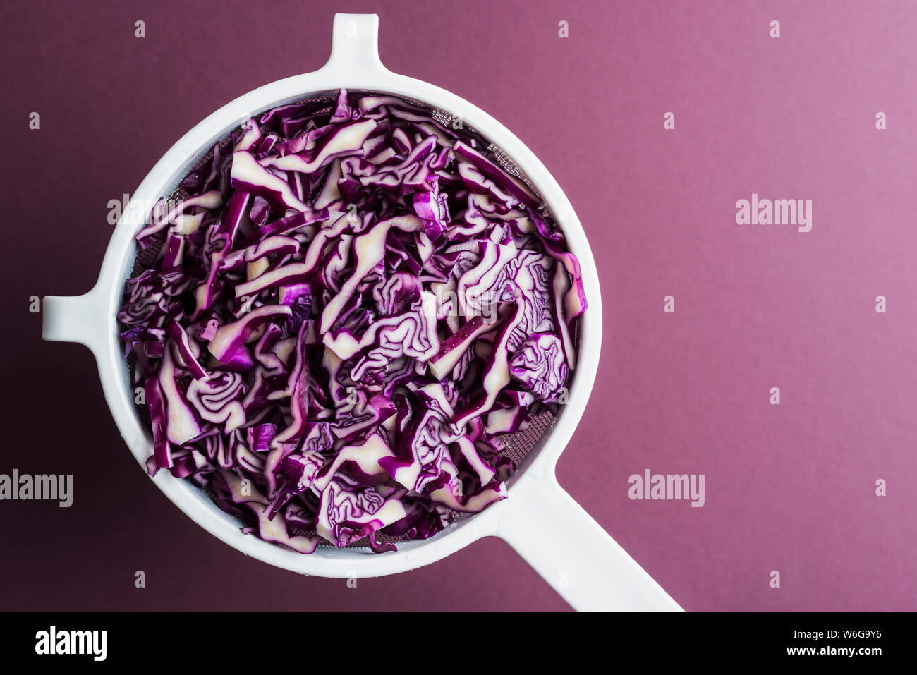 Setaccio di fettine di cavolo rosso contro uno sfondo viola. Artistico con lo spazio negativo Foto Stock