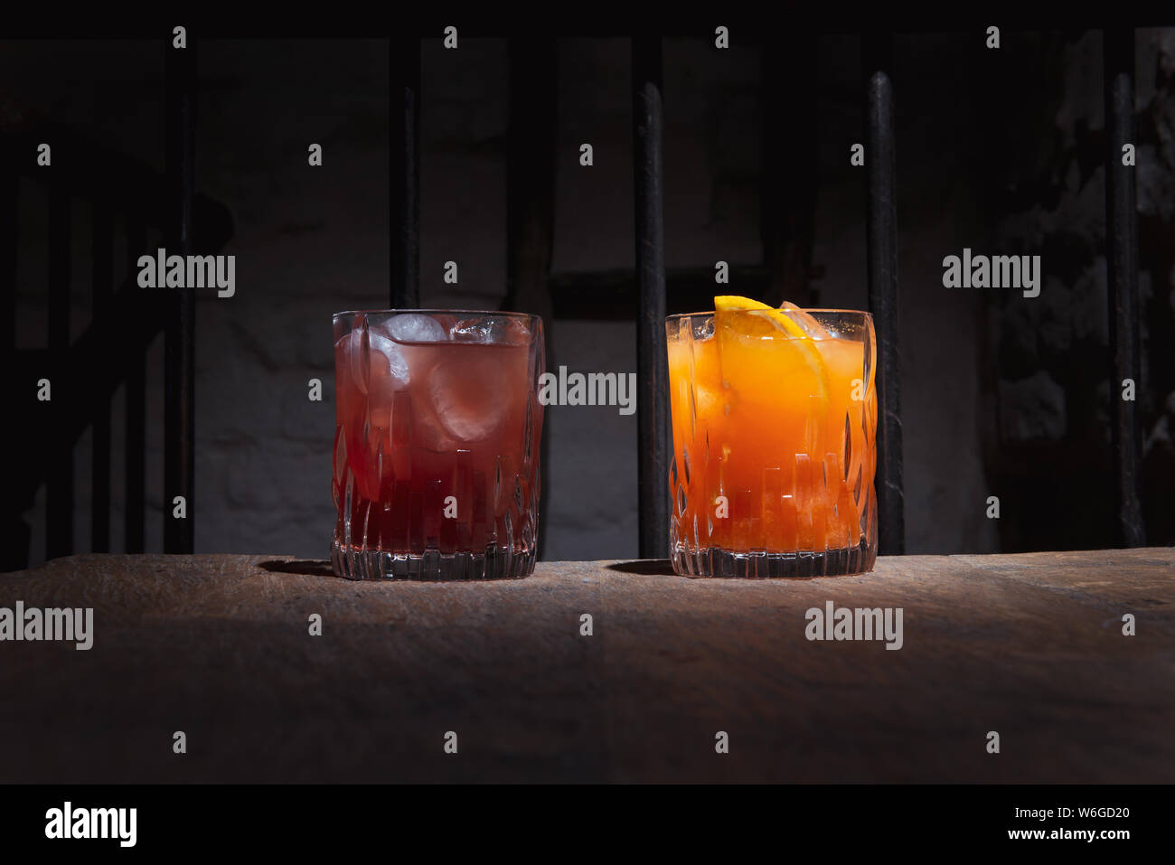 Due cocktail colorati nella barra di colore scuro. L'arancione e il rosso alcol bevande con ghiaccio su un tavolo di legno. Maschio e femmina di bere in eleganti occhiali. Foto Stock