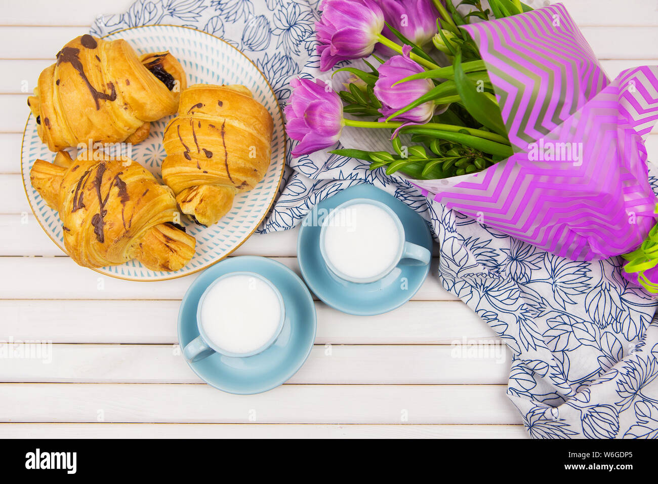 Tre croissant, due tazze di caffè sul tavolo e un mazzo di bellissimi tulipani. Foto Stock