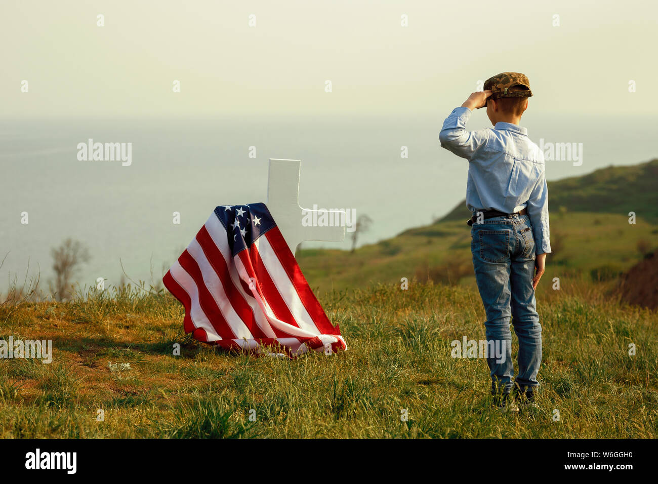 Un giovane ragazzo in un cappello militare saluta la tomba di suo padre del memorial day Foto Stock
