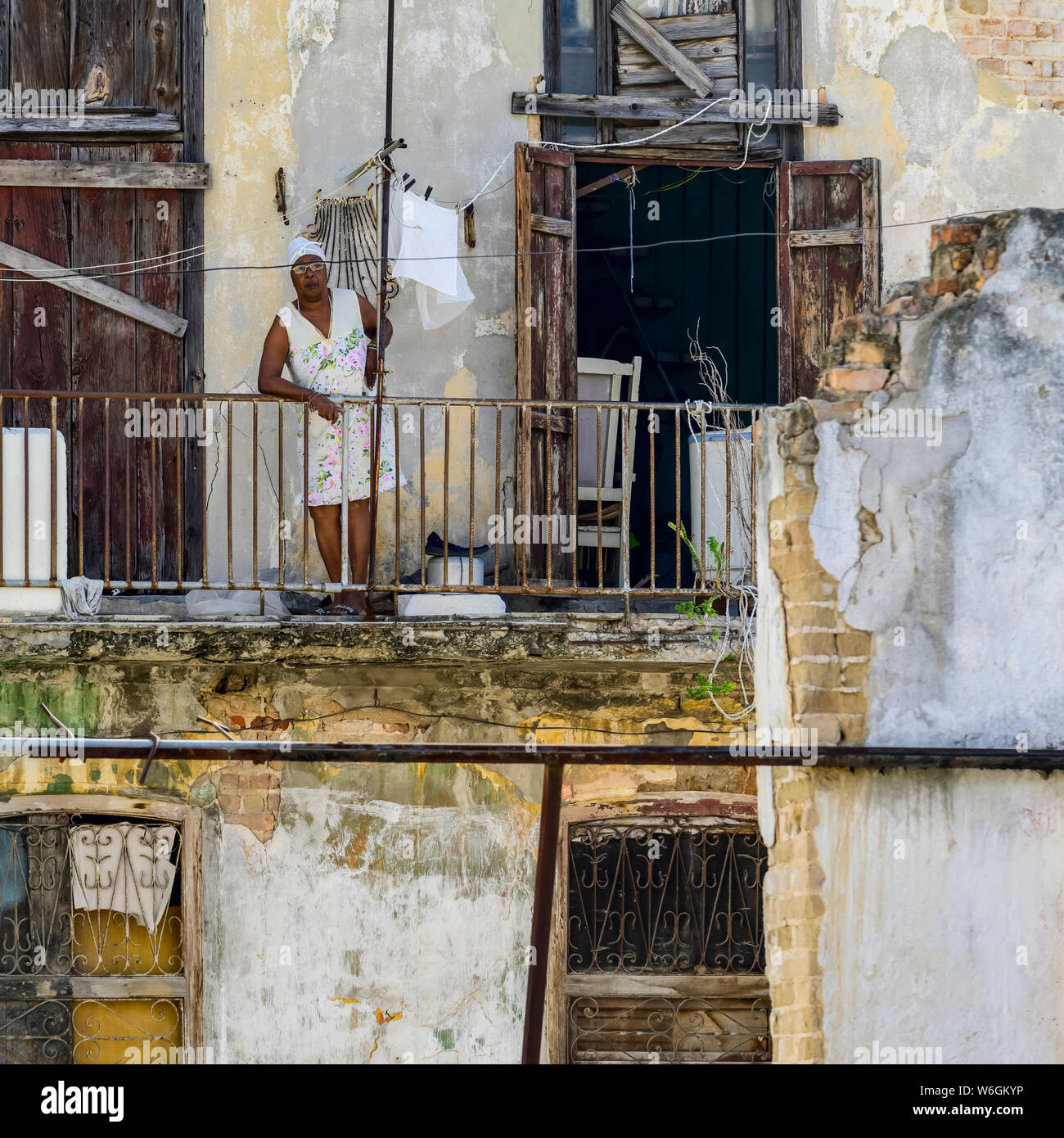 La donna sta appoggiato sulla ringhiera del suo balcone guardando giù per le strade di seguito; l'Avana, Cuba Foto Stock