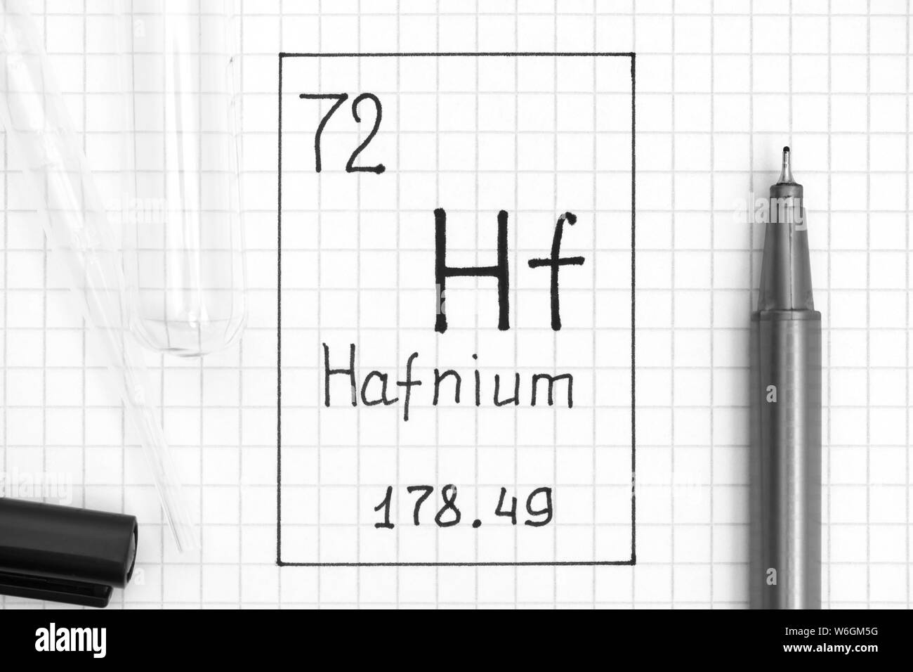 Tavola periodica degli elementi. La grafia elemento chimico afnio Hf con la penna nera, tubo di prova e la pipetta. Close-up. Foto Stock