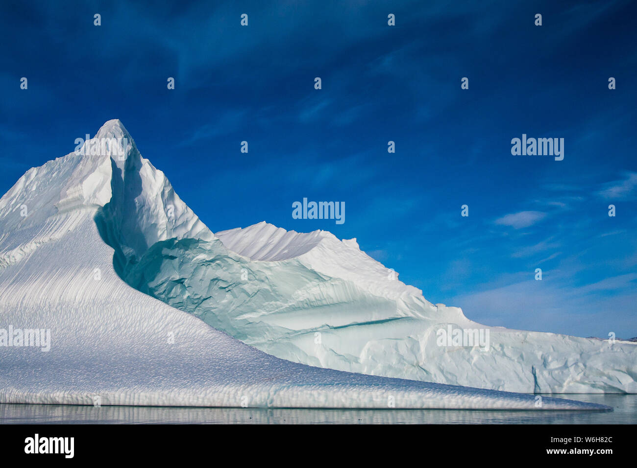 Accesa come metallica di gelato, una grande scolpita iceberg si siede sotto un ampio cielo blu in Scoresbysund, est della Groenlandia. Foto Stock