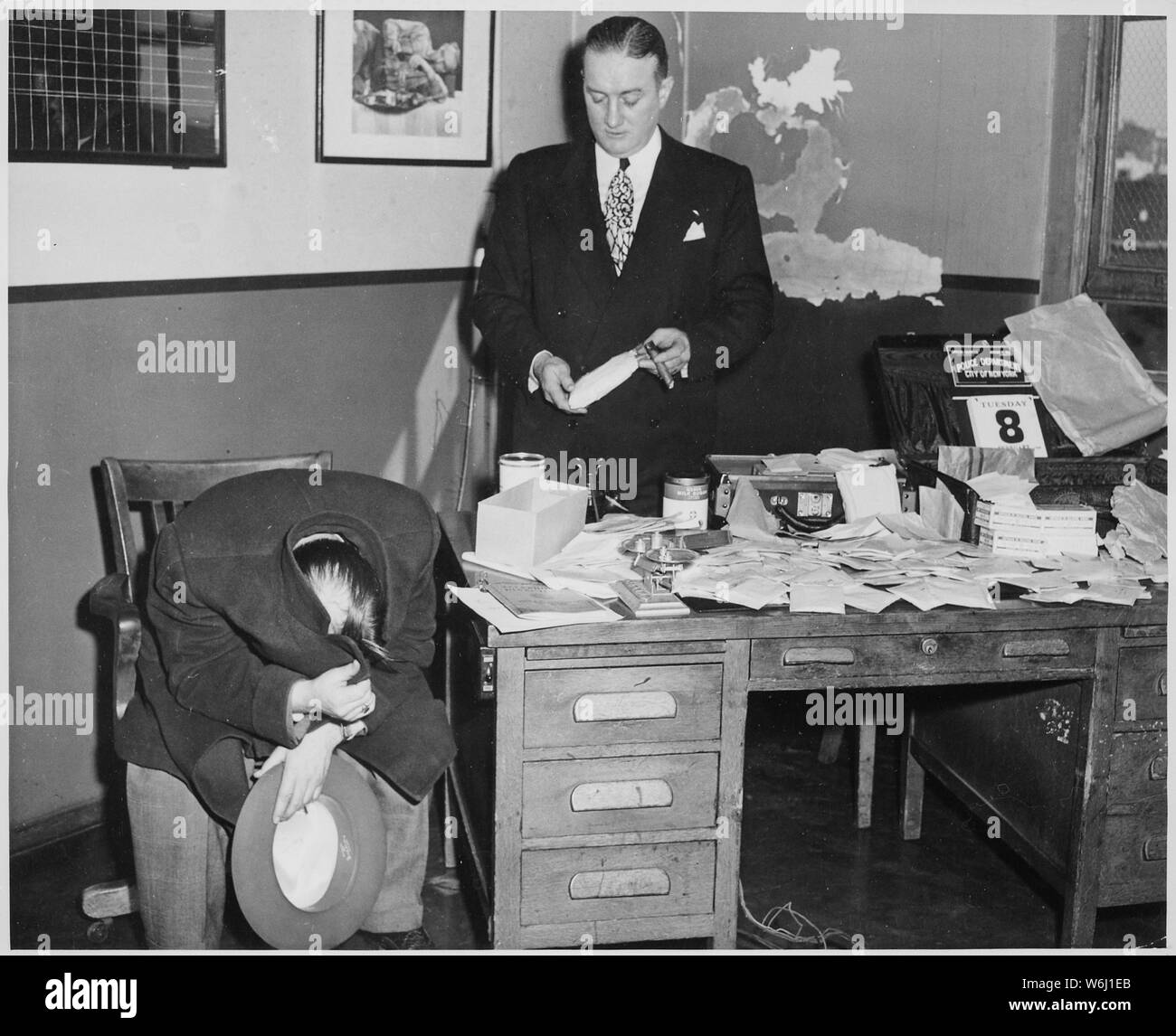 Giuseppe Basile, nasconde la sua faccia con il suo cappotto sotto arresto in connessione con il sequestro di 25 milioni di dollari che vale la pena di narcotici, 02/1949, campo di applicazione e il contenuto: Capo del detective William T. Whalen in piedi accanto a lui con alcuni dei sequestri. Foto Stock