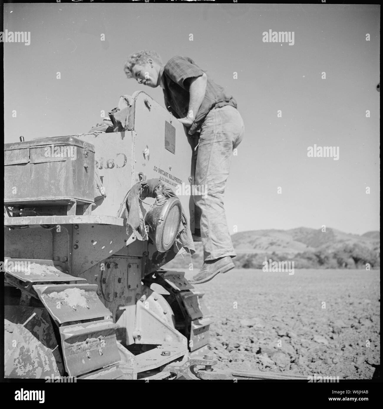 La Contea di Monterey in California. Gioventù rurale. Meccanizzazione; il settore agricolo dipendente. Caterpillar battistrada sono pericolose e alcuni cat skinners sviluppare l'abitudine di montaggio per il sedile del conducente dal sul retro Foto Stock