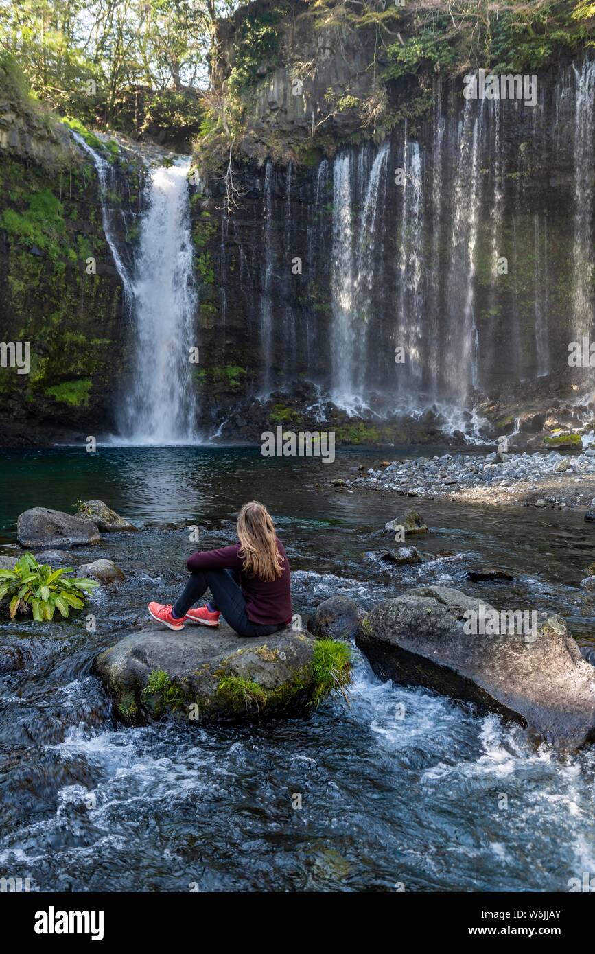Giovane donna seduta su una pietra in un fiume, Shiraito cascata, Prefettura di Yamanashi, Giappone Foto Stock