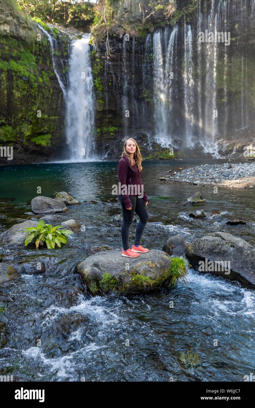 Giovane donna in piedi su una pietra in un fiume, Shiraito cascata, Prefettura di Yamanashi, Giappone Foto Stock