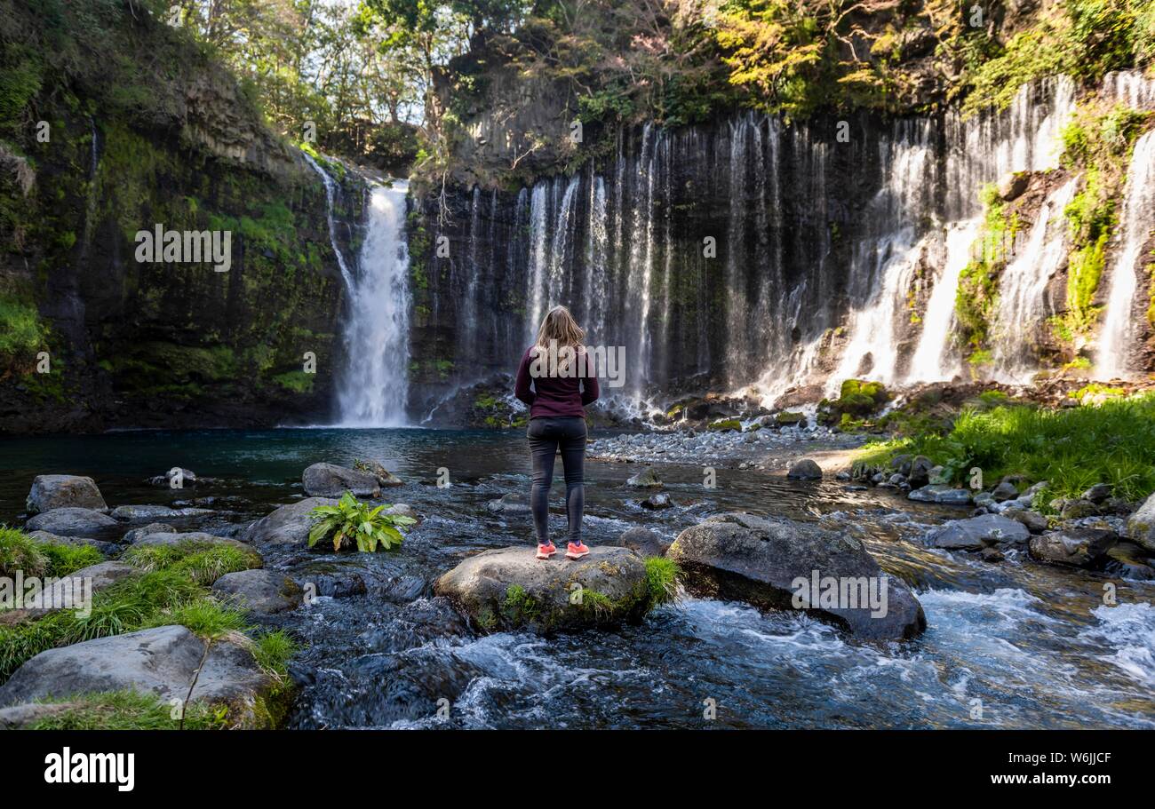 Giovane donna in piedi su una pietra in un fiume, Shiraito cascata, Prefettura di Yamanashi, Giappone Foto Stock