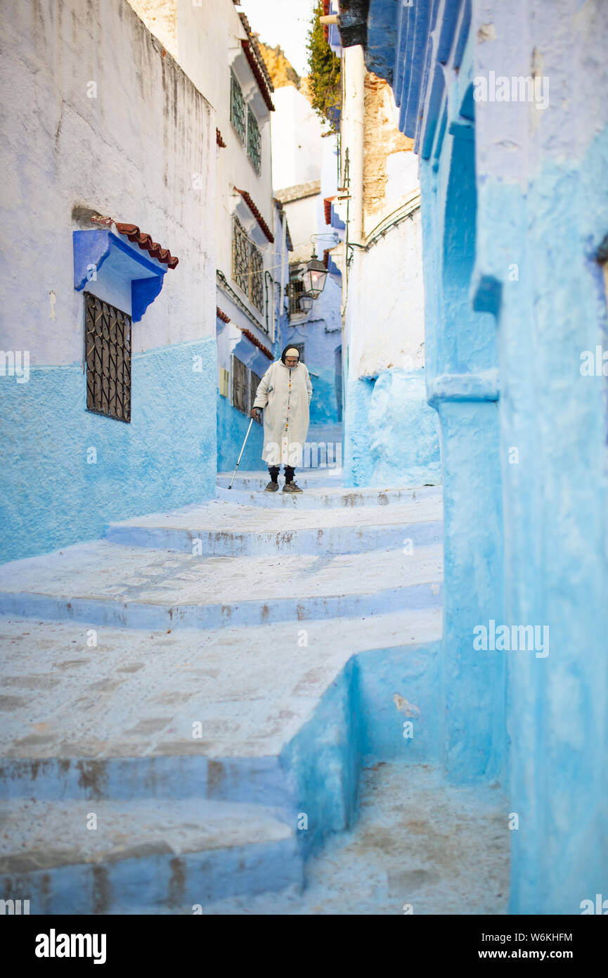 Un marocchino uomo vecchio, indossando il tradizionale Djellabah è a piedi attraverso il stretto vicoletto di Chefchaouen, Marocco. Foto Stock