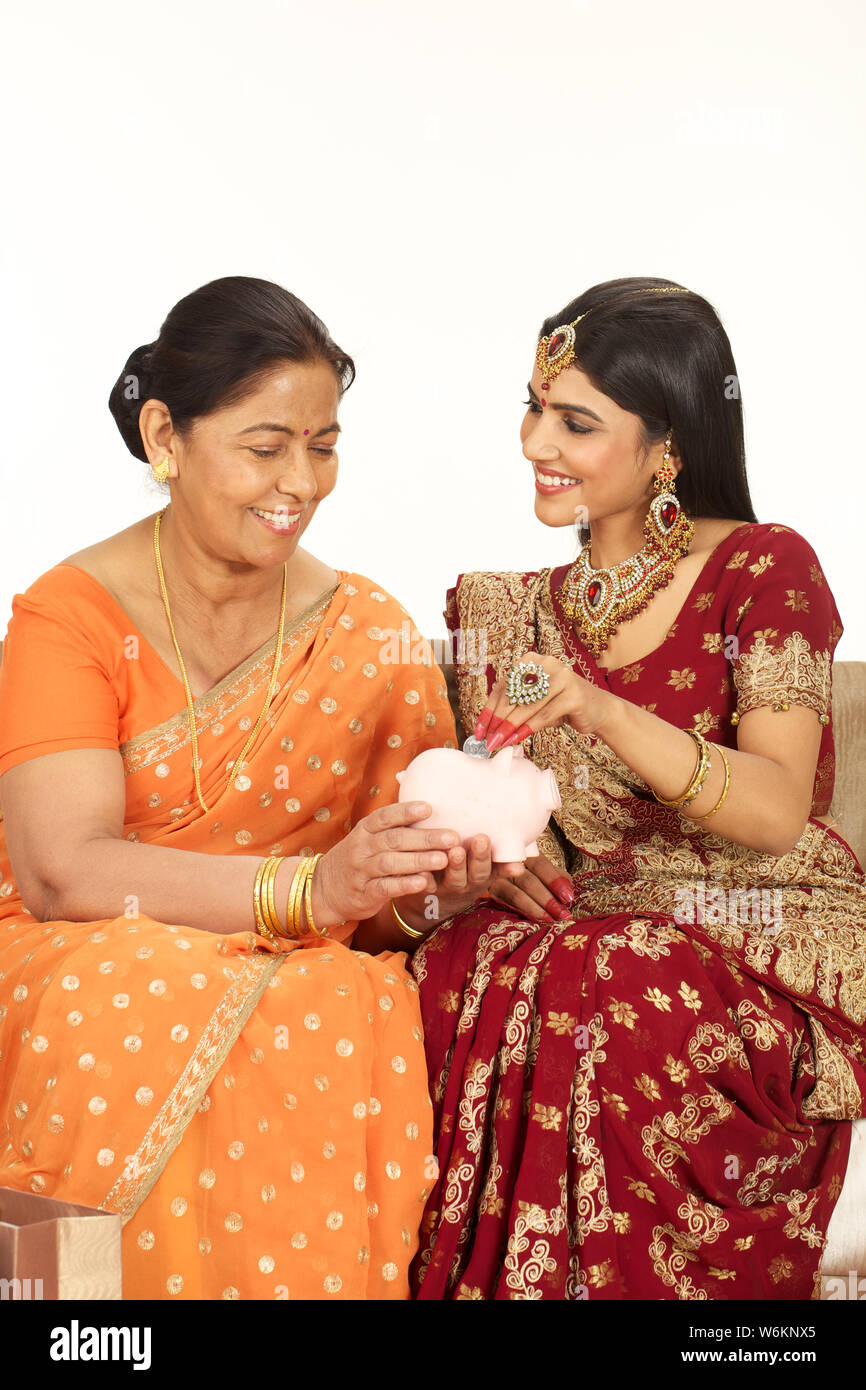 Woman putting coin into a piggy bank with her mother Foto Stock