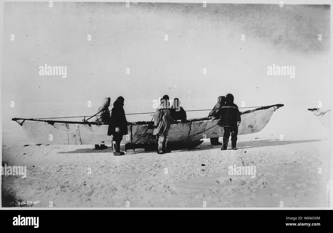 Sei eschimesi in piedi accanto a skinboat nativo (umiak) sulla slitta, punto Barrow, Alaska, 1935 Foto Stock