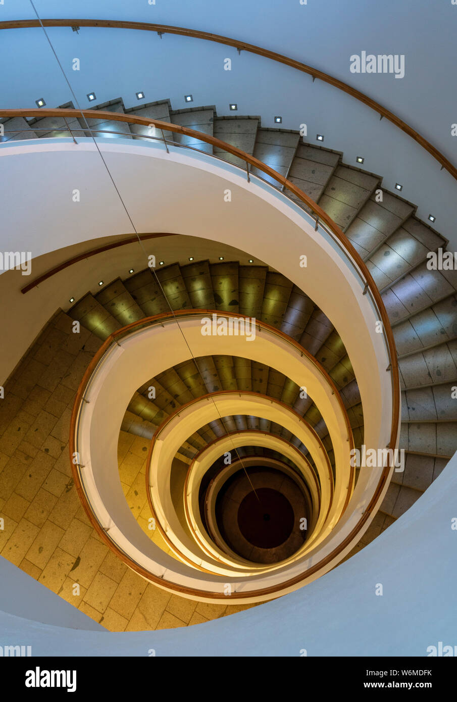 Scala a spirale conduce giù diversi piani con illuminazione drammatica. Foto Stock