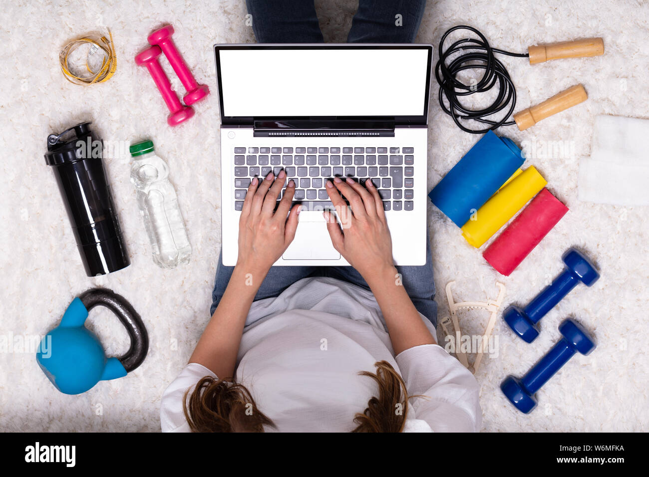 Una vista in elevazione della donna seduta sul tappeto durante l'utilizzo di laptop vicino Attrezzi Fitness Foto Stock