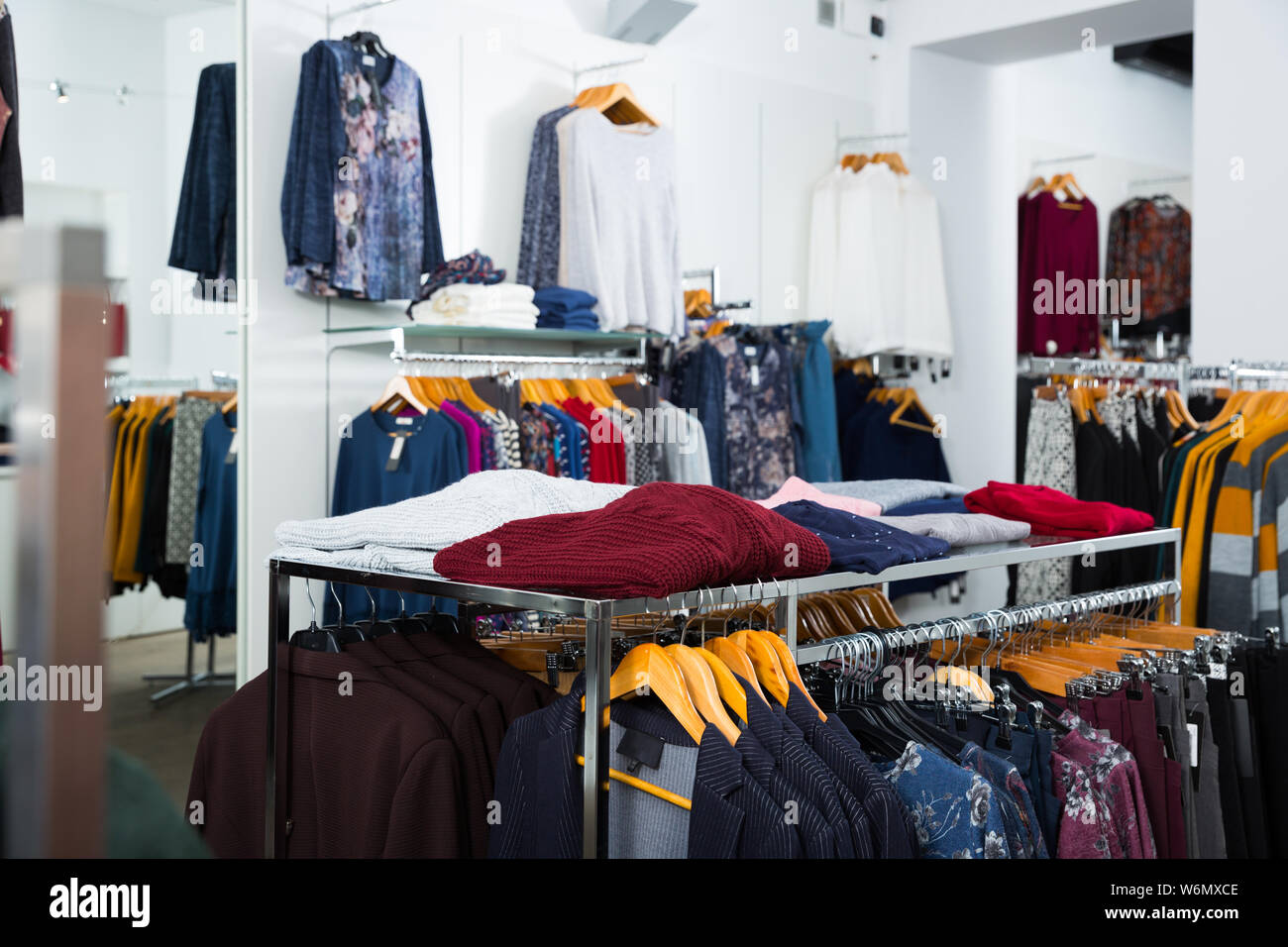 Interno del negozio di abbigliamento con le camicette e cardigan su grucce e piani di appoggio Foto Stock