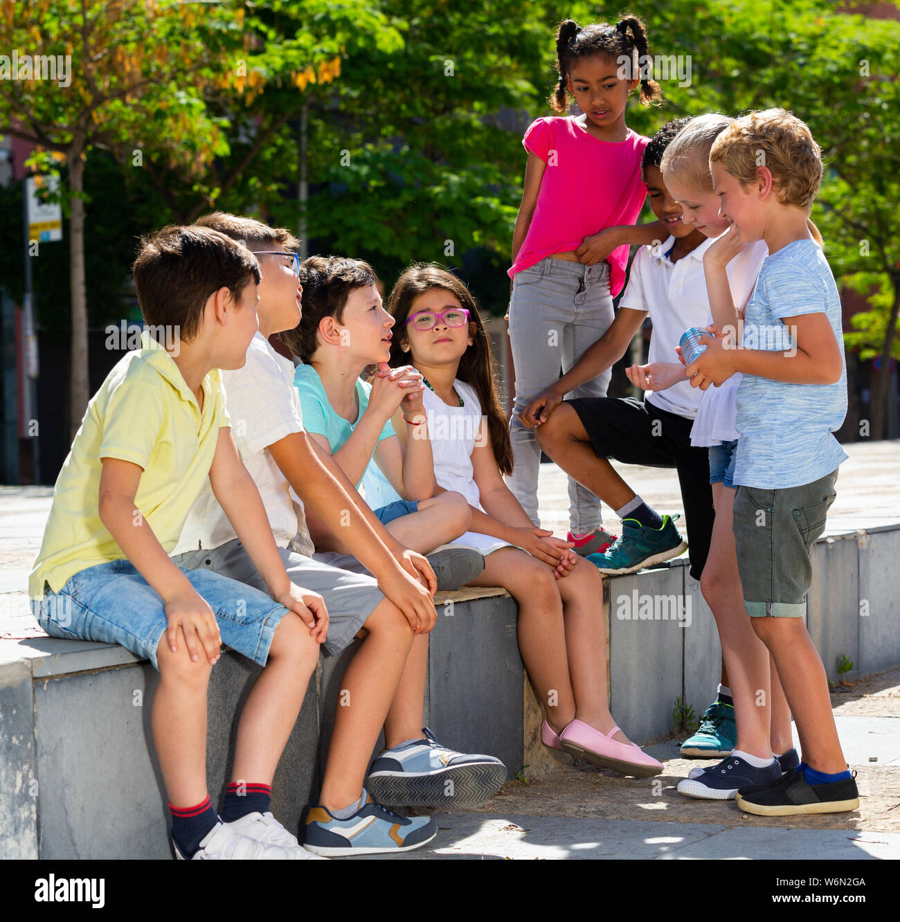 Il gruppo di allegro bambini seduti su un banco di lavoro e la condivisione di segreti all'aperto Foto Stock
