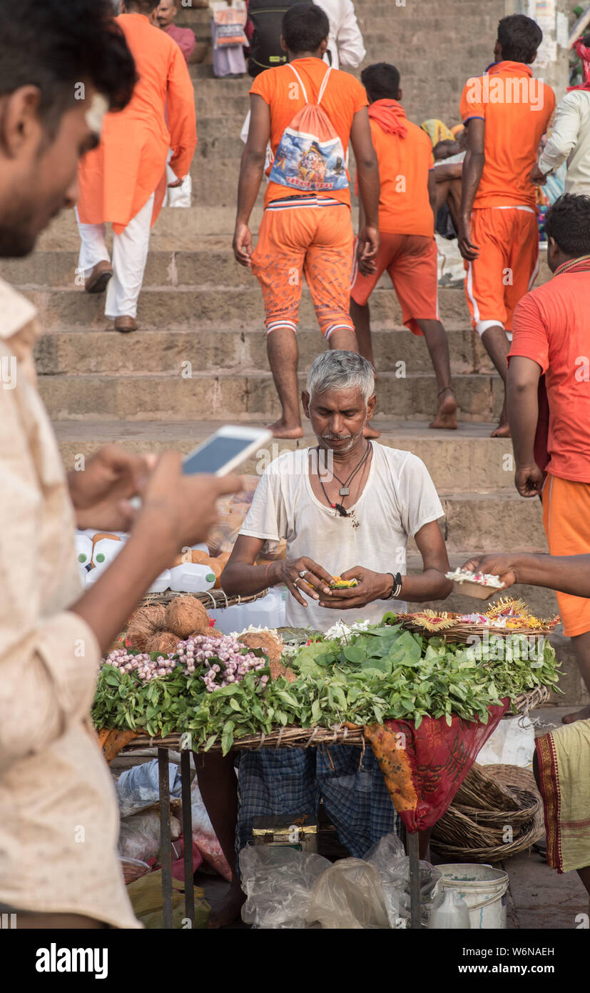 Un uomo indiano che vendono fiori per le offerte di puja mentre un uomo con uno smartphone è in primo piano Foto Stock