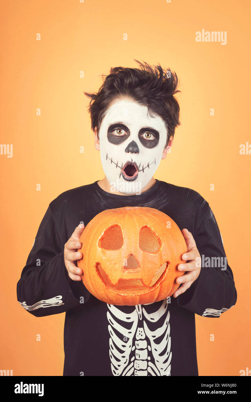 Happy Halloween.divertente bambino in un costume di scheletro con zucca di Halloween contro lo sfondo arancione Foto Stock