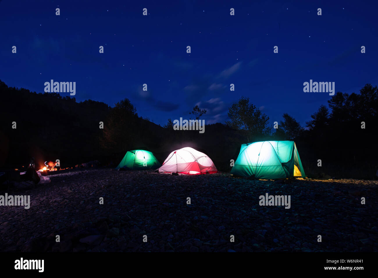 Notte Campeggio. Illumina le tende e Il Falò in montagna sotto il cielo notturno con stelle. vicino alla foresta Foto Stock