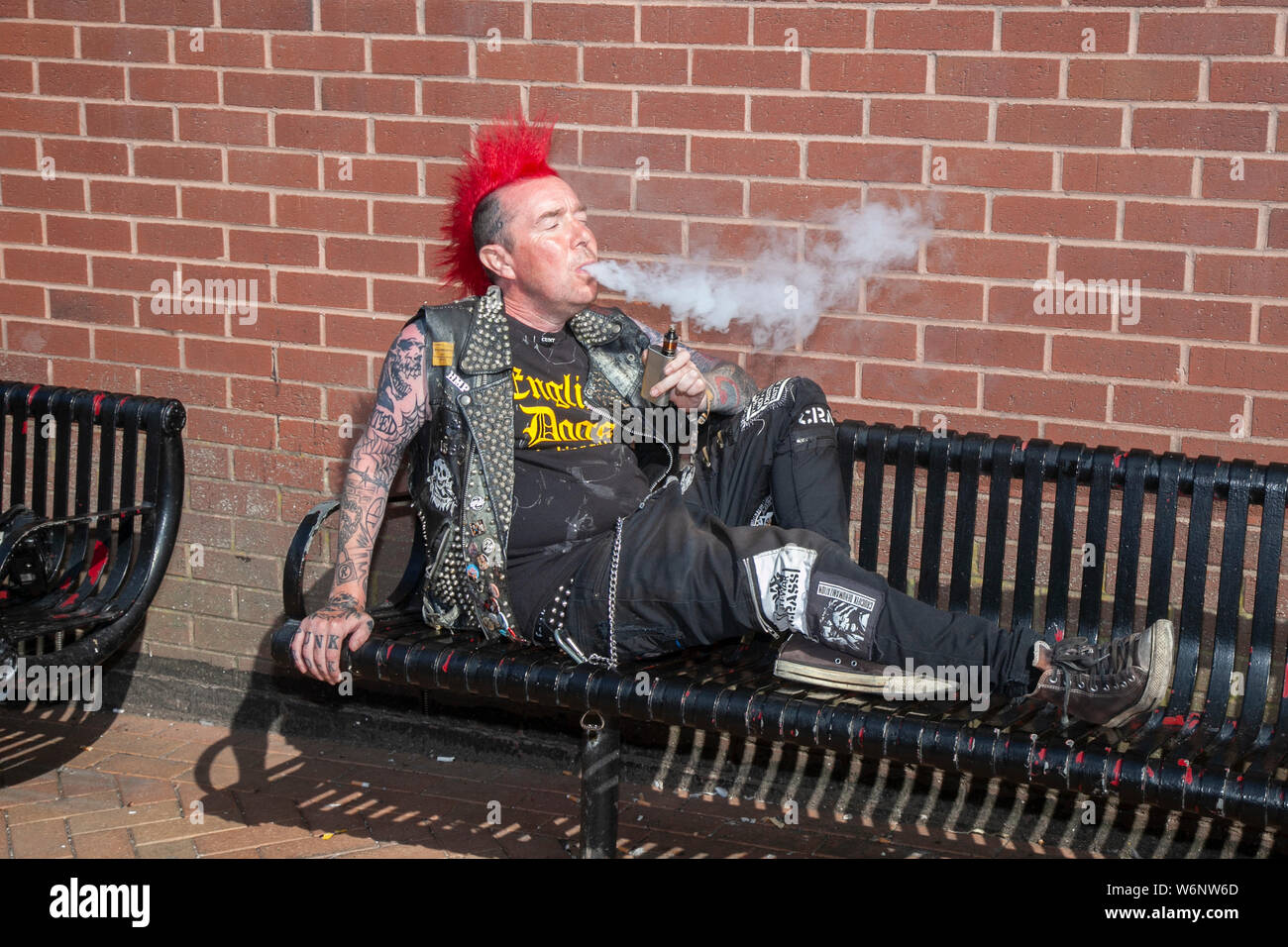 Punk rocker con taglio di capelli rosso mohican godendo di un fumo a Blackpool, Lancashire, Regno Unito. Ago, 2019. Lee Talbot di Leeds al Rebellion Festival, il più grande festival punk del mondo a Blackpool. All'inizio di agosto, i Blackpool's Winter Gardens ospitano una massiccia serie di punk band per la 21a edizione del Rebellion Festival che attrae migliaia di turisti nel resort. Foto Stock