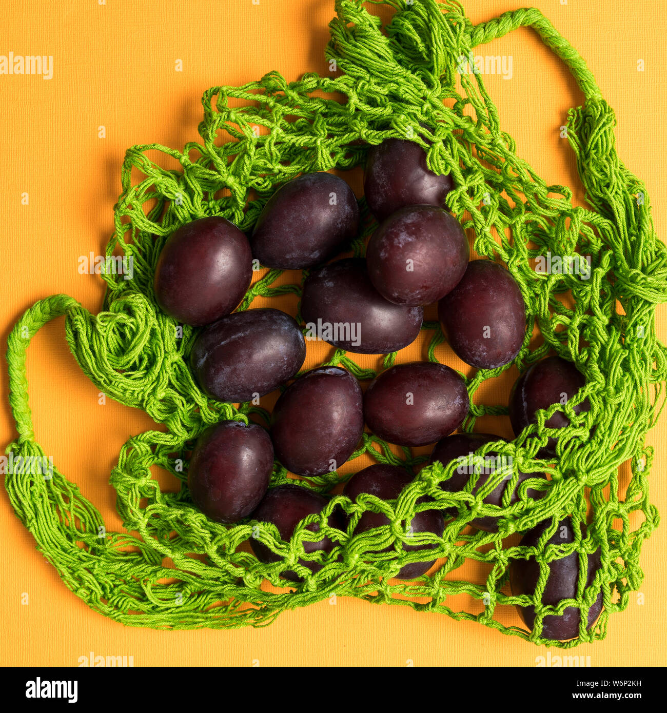 Appartamento laici prugne fresche nell'eco riutilizzabili rifiuti zero mesh stringa shopping bag su sfondo giallo, orientamento quadrati. Foto Stock