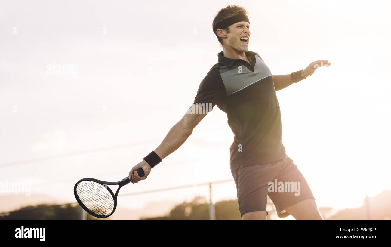 Giovane giocatore giocare a tennis su hard court in una giornata di sole. Giocatore di tennis professionista colpendo un diretti vincitore durante una partita. Foto Stock