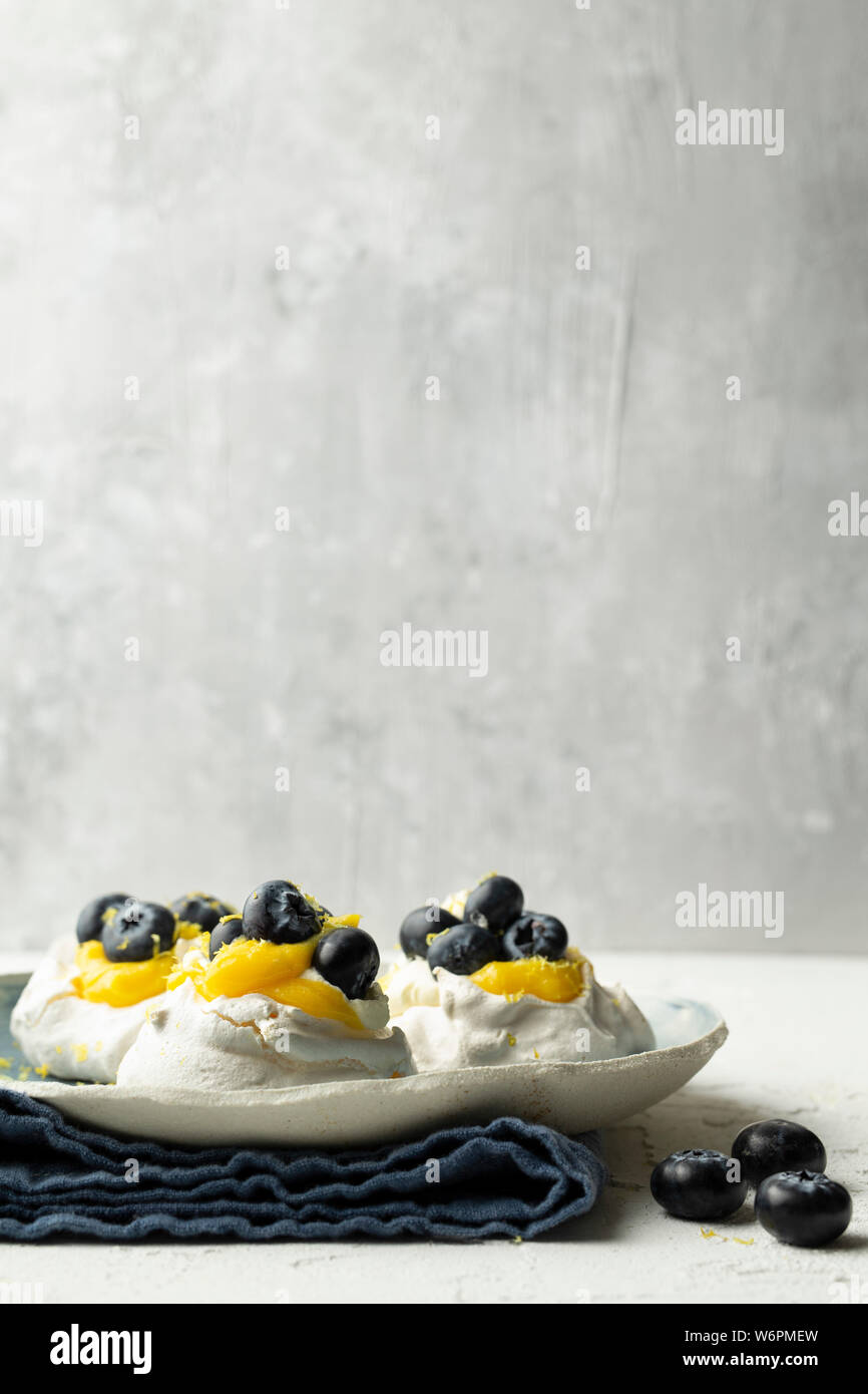 Meringhe con cagliata di limone e mirtilli su un lato piastra realizzata in appoggio su un lino blu igienico. Foto Stock