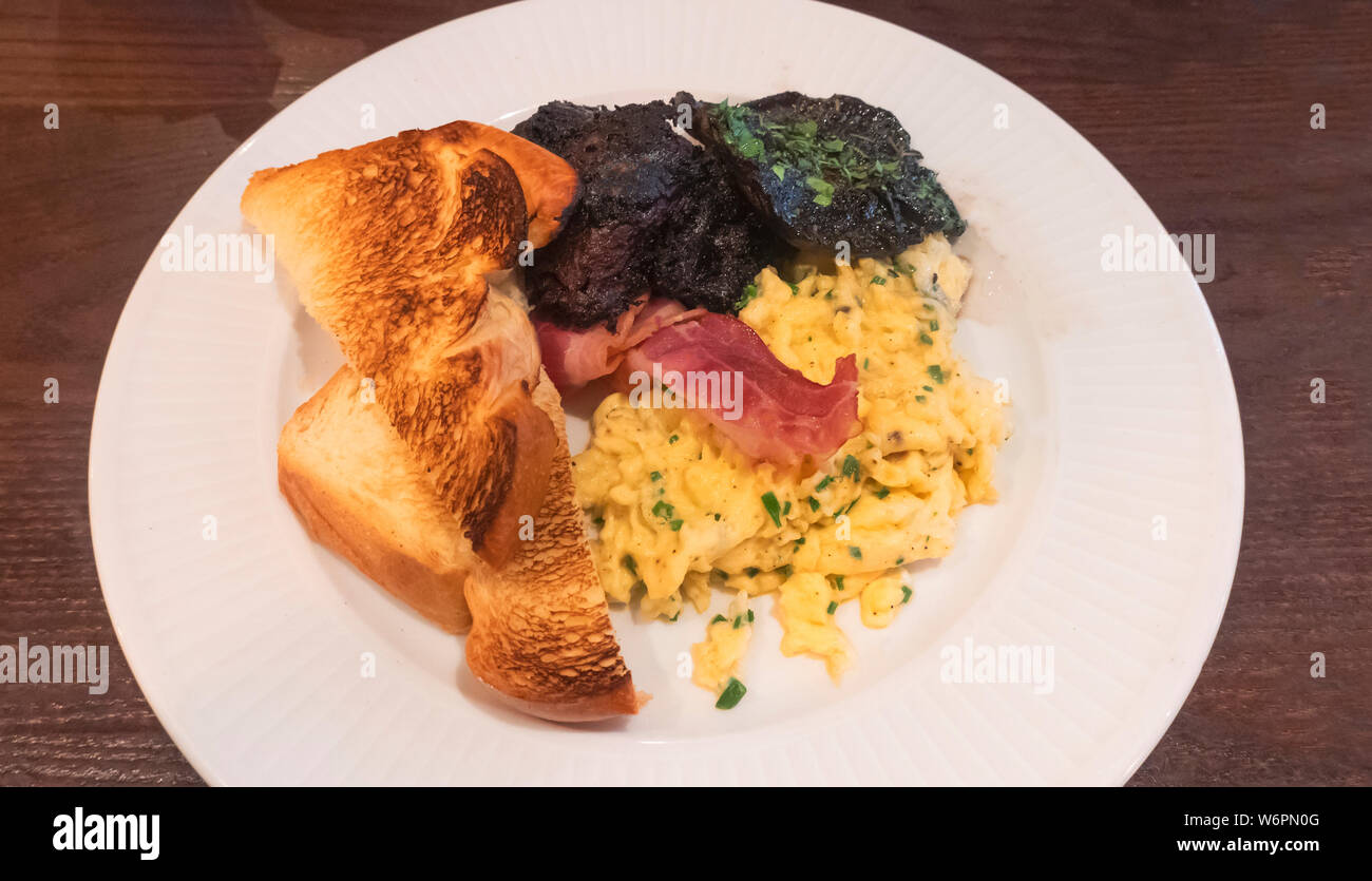 Una classica colazione francese -- uova strapazzate con erba cipollina, pancetta, funghi, Boudin Noir e pane tostato Foto Stock