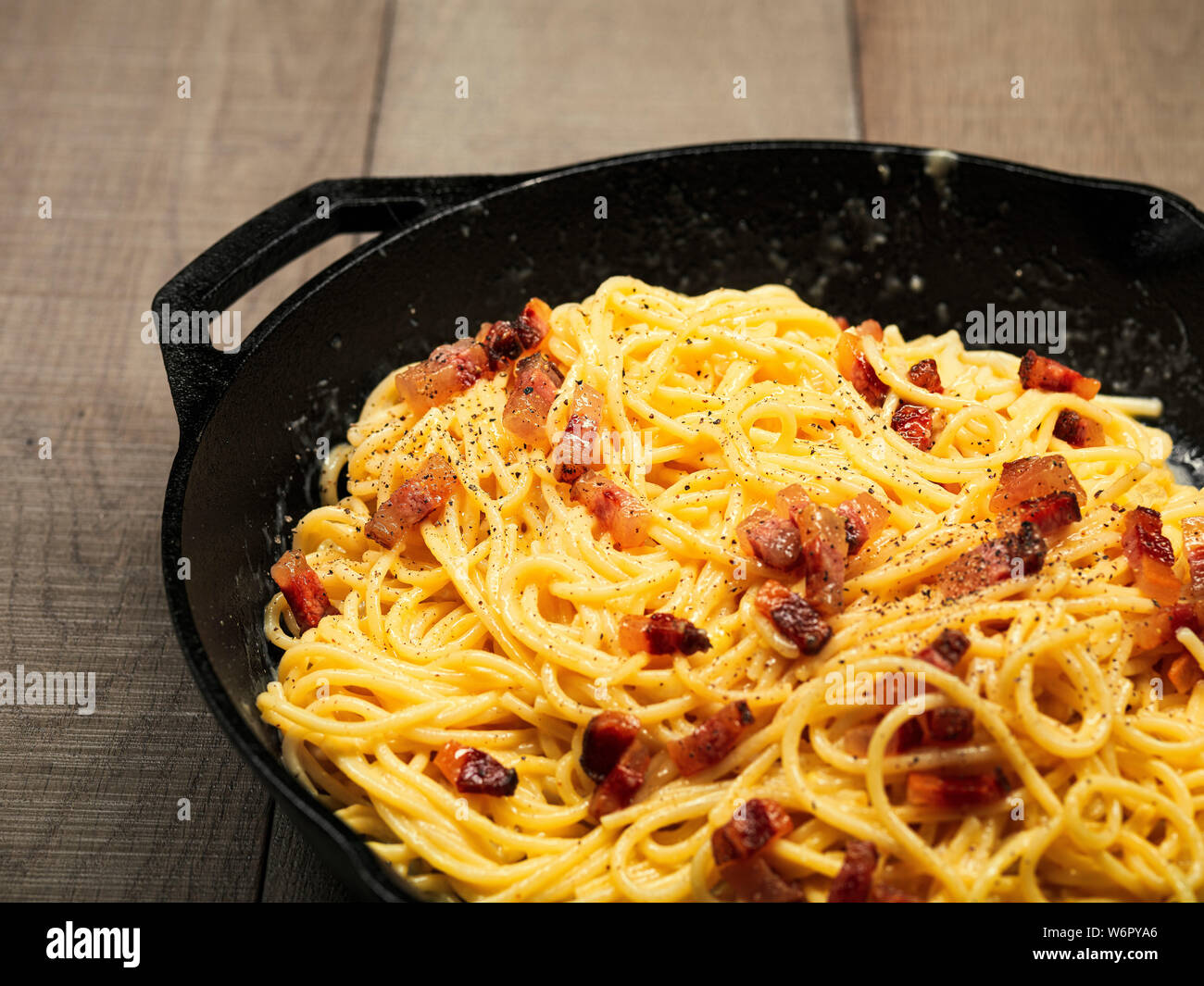 L'italiano "paghetti alla carbonara' con pancetta, uova e pepe cucinati e serviti in una ghisa panoramica su una tavola di legno Foto Stock