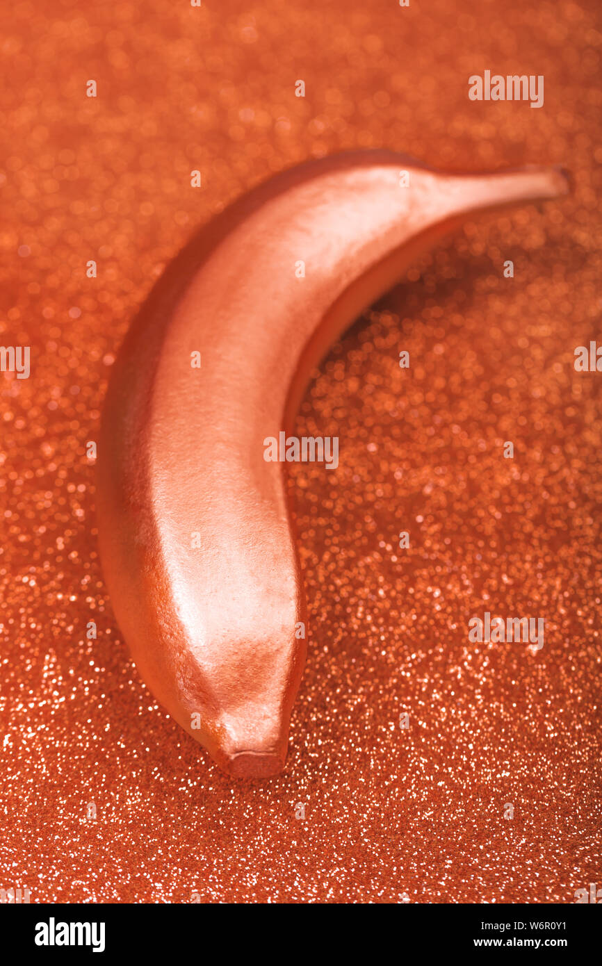 Color bronzo del cibo in metallo, banana metallico su glitter o shimmer sfondo. Elegante appartamento tropicale laici. Concetto creativo, orietntation verticale Foto Stock