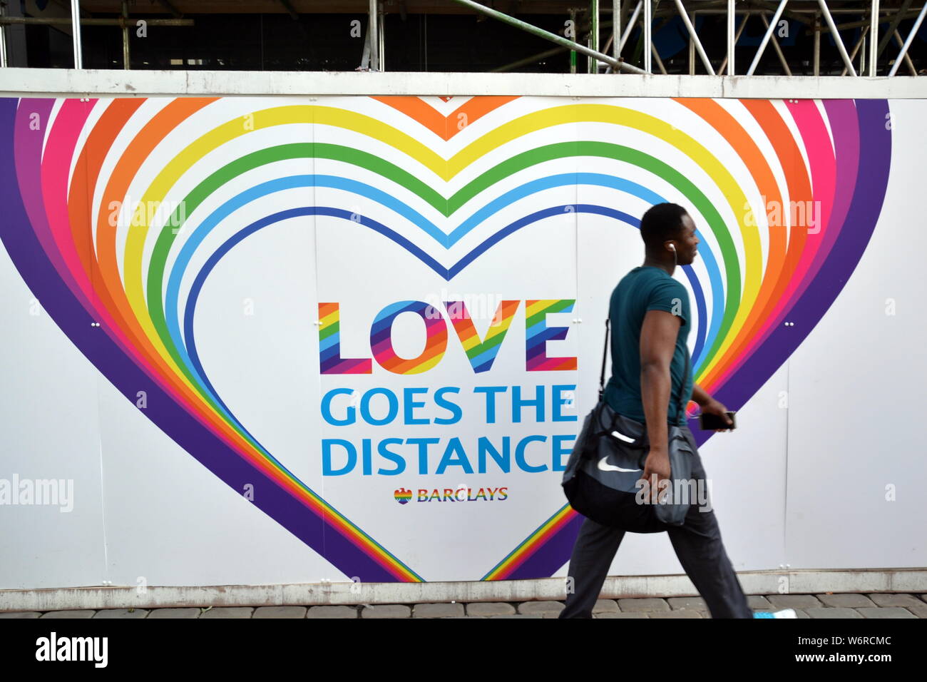 Un uomo cammina passato un arcobaleno themed 'l'amore passa la distanza " segno su Barclays Bank, Market Street, Manchester, UK, durante l orgoglio lgbt periodo Foto Stock