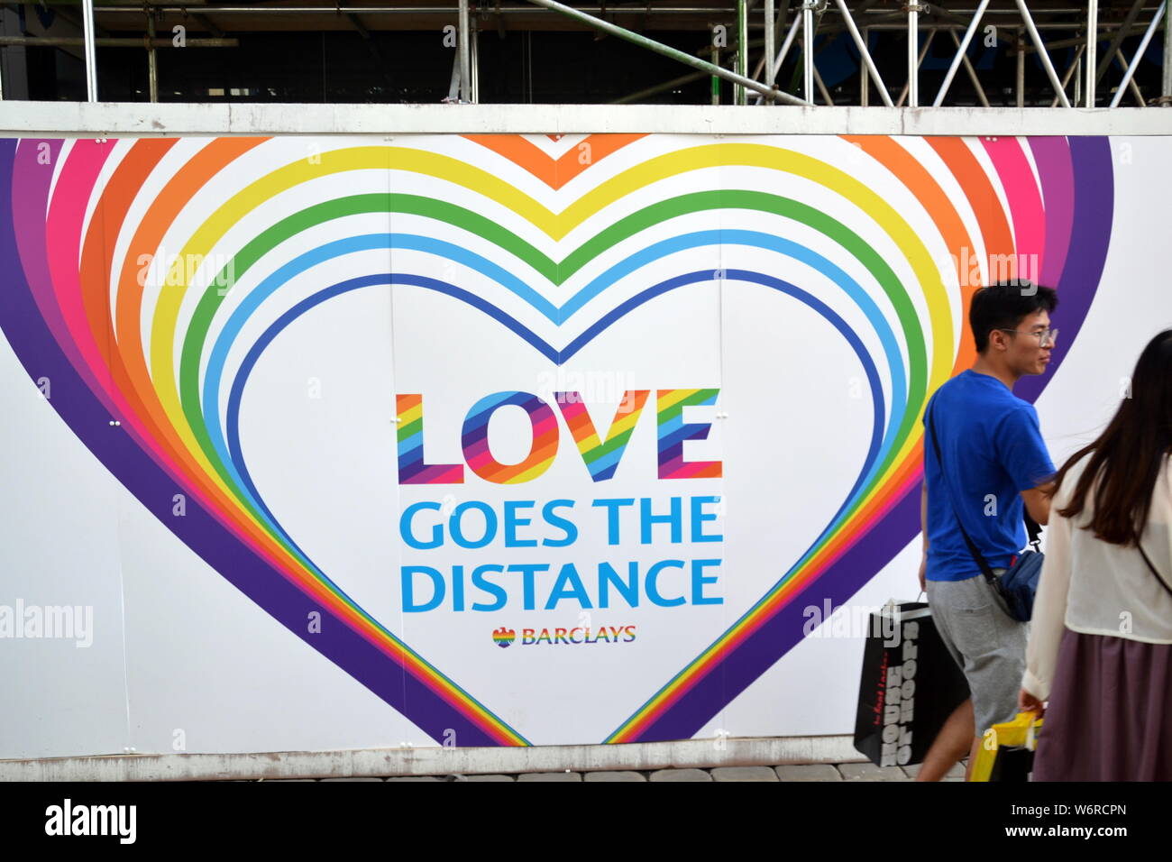 Passerelle-a piedi davanti a un cartello a tema arcobaleno "Love Goes the Distance" sulla Barclays Bank, Market Street, Manchester, Regno Unito, durante il periodo di orgoglio lgbt Foto Stock