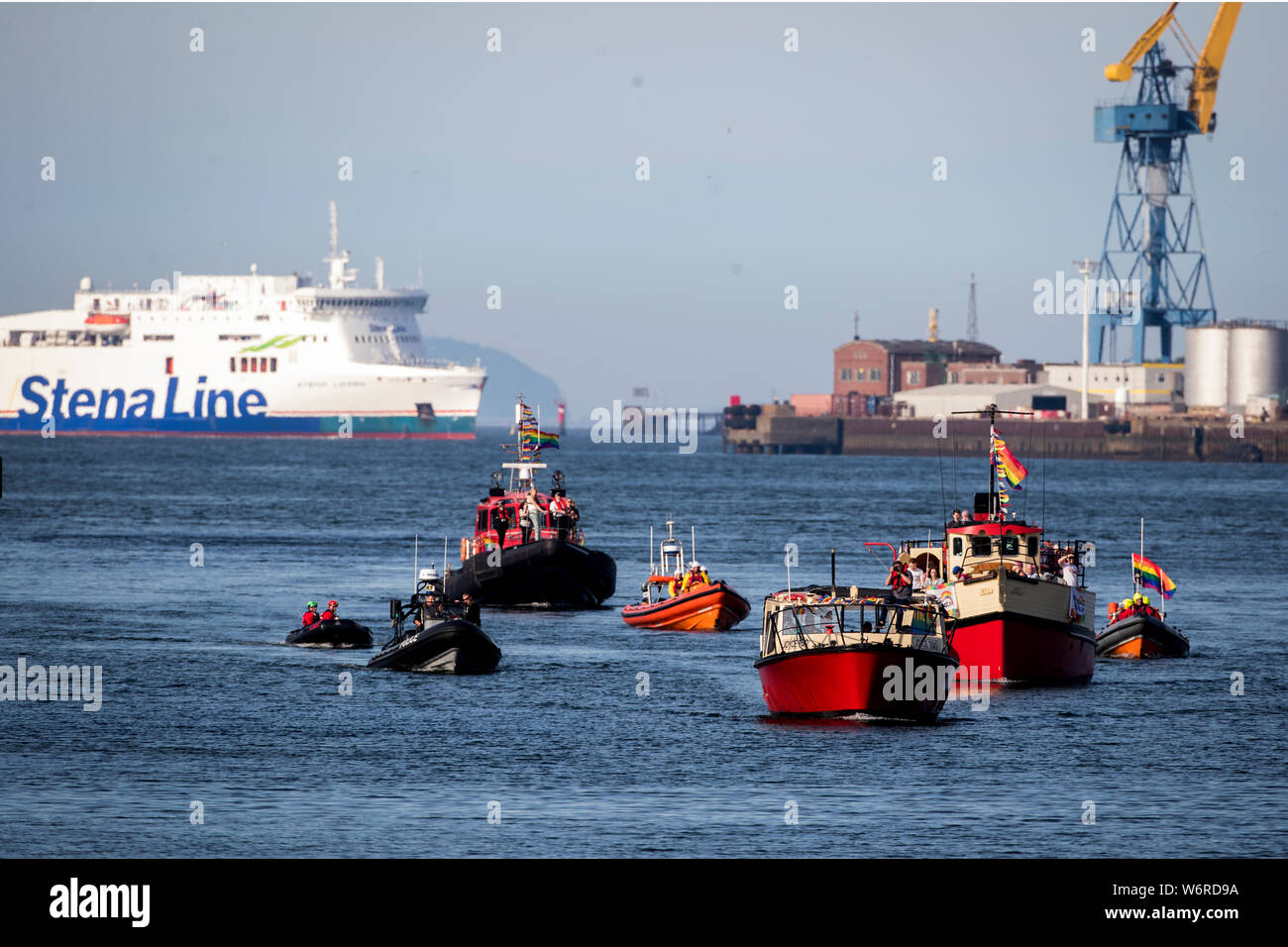 Flottiglie di navi portando bandiere arcobaleno in Belfast come essi sail dalla bocca di porto di Belfast fino al fiume Lagan, prima di una presentazione a Belfast Lord Mayor John Finucane con la prima bandiera di orgoglio che volerà dal Municipio, precedendo il Belfast Pride Parade di sabato. Foto Stock