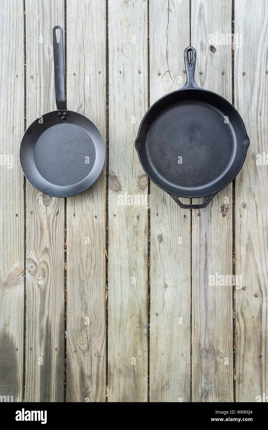 Tradizionale vs nuovo pentole battaglia - ghisa versus acciaio al carbonio o in teflon. Sfondo di legno. Più sano utensile di cottura opzioni. Vuoto testo vuoto r Foto Stock