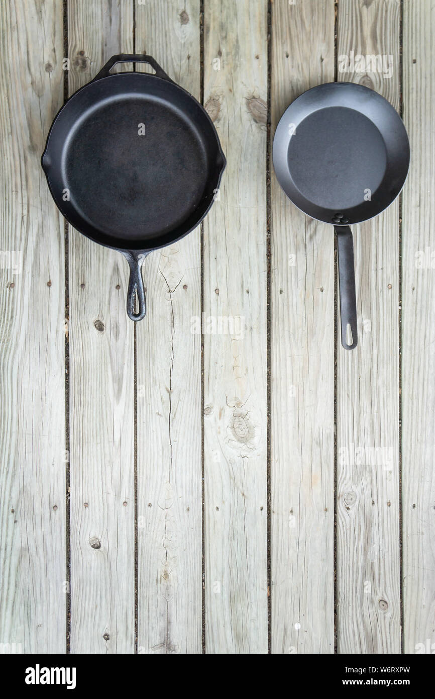 Tradizionale vs nuovo pentole battaglia - ghisa versus acciaio al carbonio o in teflon. Sfondo di legno. Più sano utensile di cottura opzioni. Vuoto testo vuoto r Foto Stock