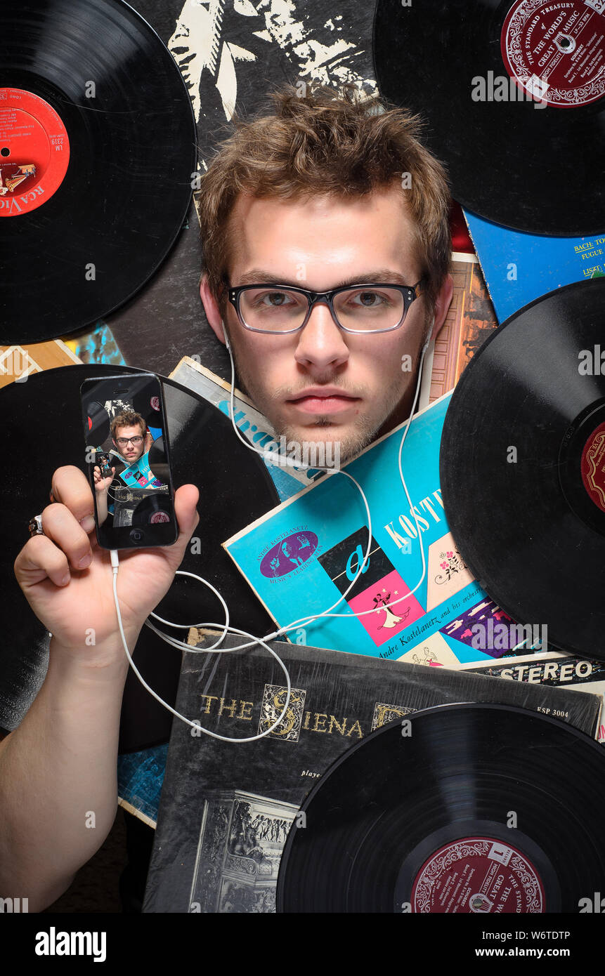 Venti-qualcosa maschio caucasico sepolto sotto una selezione di vecchi dischi in vinile album, tenendo un smartphone con questa fotografia visualizzata sulla sua parte anteriore. Foto Stock