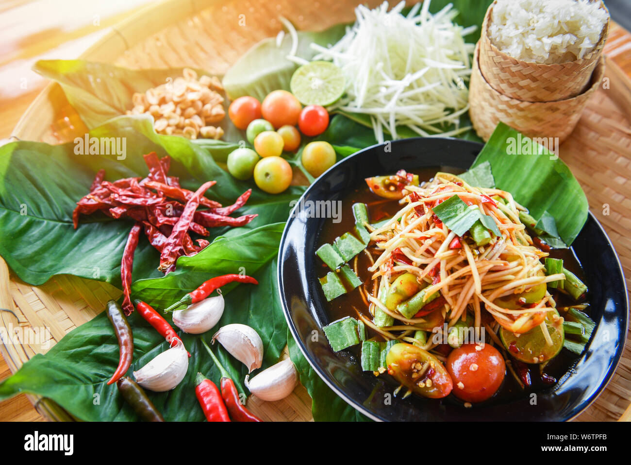 Insalata di papaia servita sul tavolo da pranzo in legno / papaia verde insalata thai piccante cibo sulla piastra con riso appiccicoso erbe e spezie ingredienti con peperoncino tom Foto Stock
