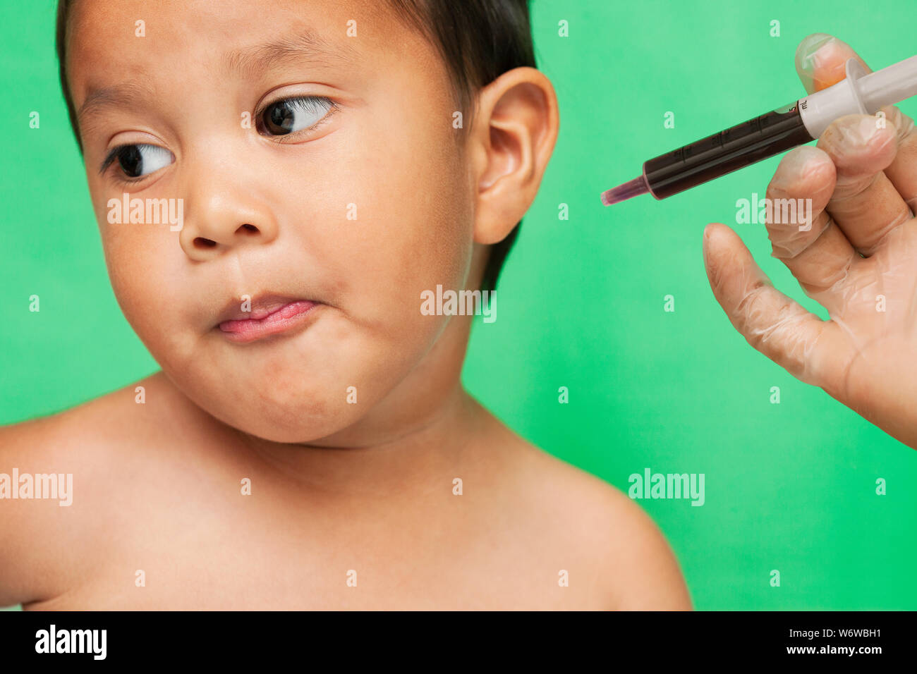 Un bambino di 3 anni bambino rifiutando di prendere per via orale di farmaci di uve per l'influenza da un medico professionista. Foto Stock